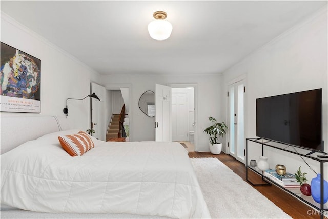 bedroom with connected bathroom, wood finished floors, and ornamental molding