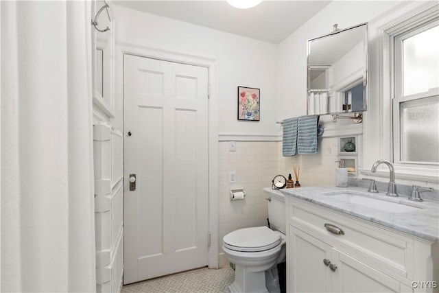 bathroom featuring vanity, tile walls, toilet, and a wainscoted wall