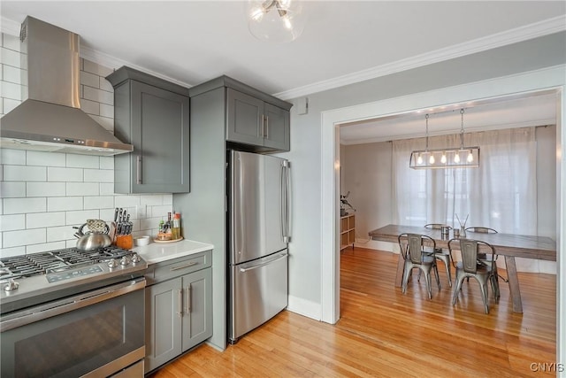 kitchen featuring ornamental molding, gray cabinetry, stainless steel appliances, wall chimney exhaust hood, and light wood-type flooring