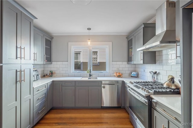 kitchen with wall chimney range hood, light countertops, gray cabinets, appliances with stainless steel finishes, and a sink