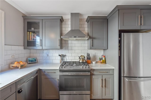 kitchen featuring gray cabinetry, appliances with stainless steel finishes, wall chimney exhaust hood, light countertops, and decorative backsplash