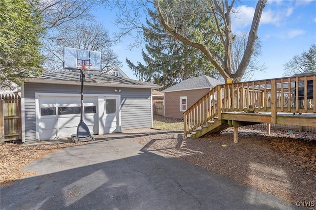 exterior space featuring fence, a wooden deck, a garage, an outbuilding, and driveway