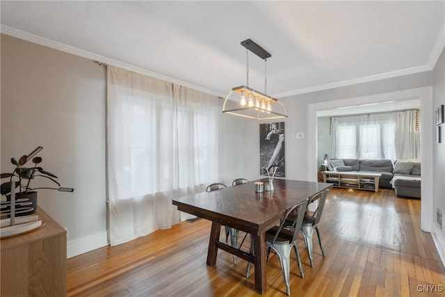 dining area with wood-type flooring, baseboards, and ornamental molding