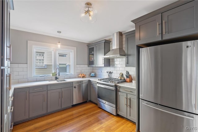 kitchen featuring gray cabinets, a sink, light countertops, appliances with stainless steel finishes, and wall chimney exhaust hood