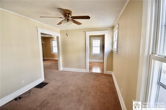 carpeted spare room featuring visible vents, ceiling fan, baseboards, and ornamental molding