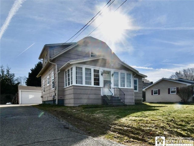 bungalow-style home featuring driveway, a detached garage, an outbuilding, and a front yard