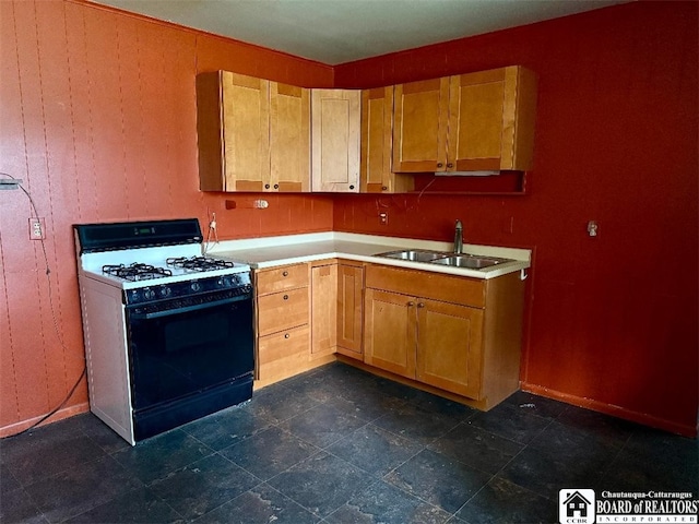 kitchen featuring a sink, wooden walls, gas range, light countertops, and baseboards