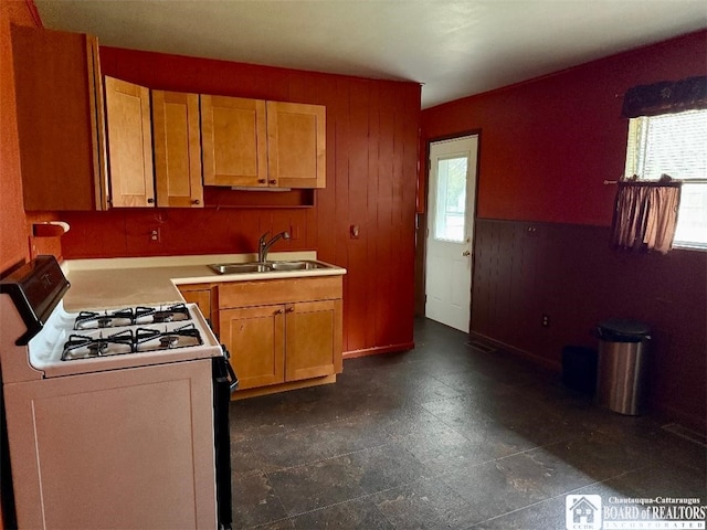 kitchen featuring wooden walls, a wainscoted wall, a sink, light countertops, and white gas range oven