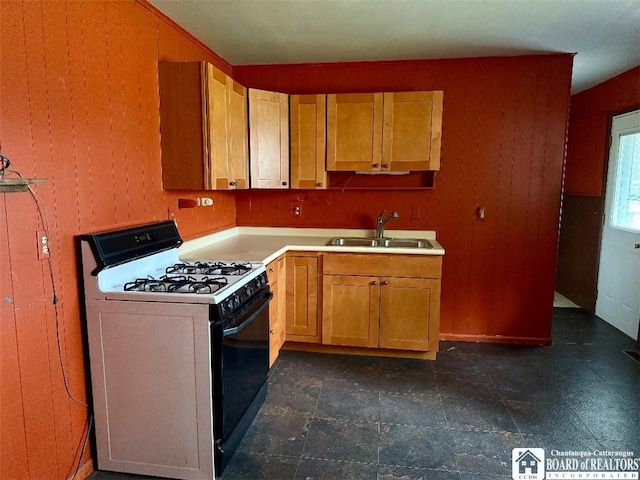 kitchen featuring range with gas stovetop, light countertops, wooden walls, and a sink