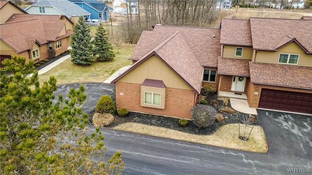 view of front facade with brick siding, a residential view, driveway, and roof with shingles