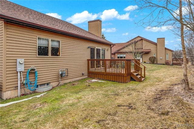 back of house with a wooden deck, a chimney, a yard, and roof with shingles