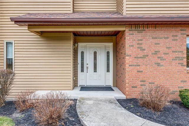 property entrance with brick siding and a shingled roof