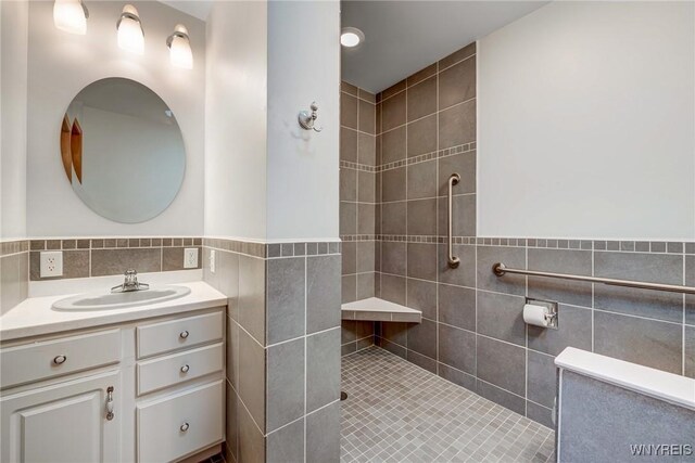 full bathroom featuring a wainscoted wall, tile walls, vanity, and a tile shower