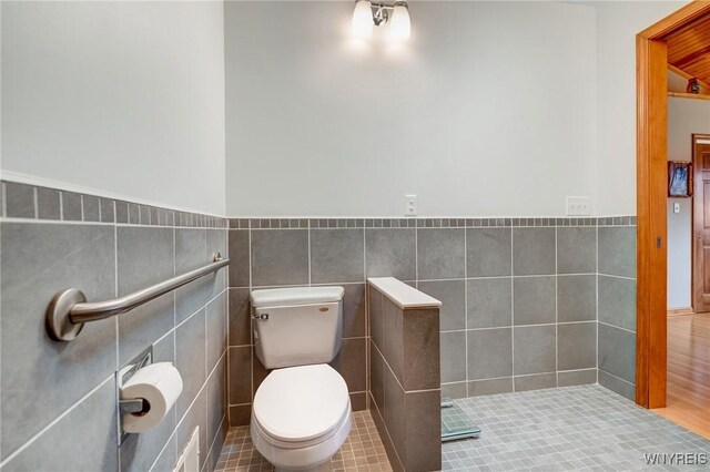 bathroom with tile walls, toilet, a wainscoted wall, and tile patterned floors