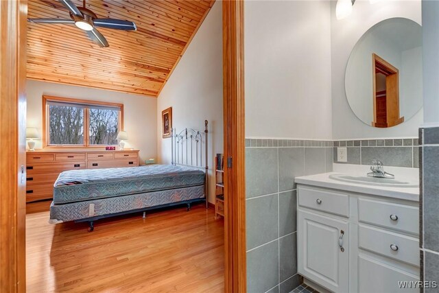 bedroom with light wood-type flooring, vaulted ceiling, wooden ceiling, tile walls, and a sink