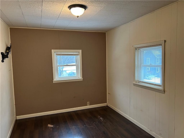 unfurnished room featuring baseboards and dark wood-type flooring