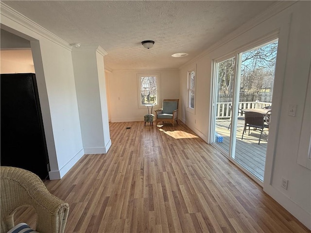 sitting room with ornamental molding, baseboards, light wood-type flooring, and a textured ceiling