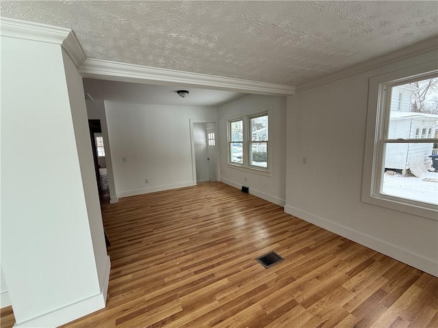 unfurnished room featuring crown molding, a wealth of natural light, visible vents, and light wood finished floors