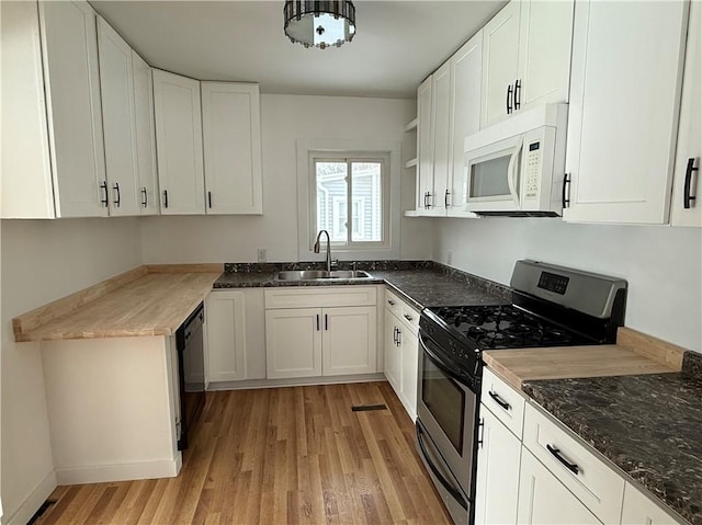 kitchen featuring gas stove, white microwave, a sink, white cabinets, and light wood-style floors