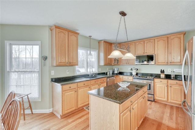 kitchen with light wood finished floors, light brown cabinets, a kitchen island, stainless steel appliances, and a sink