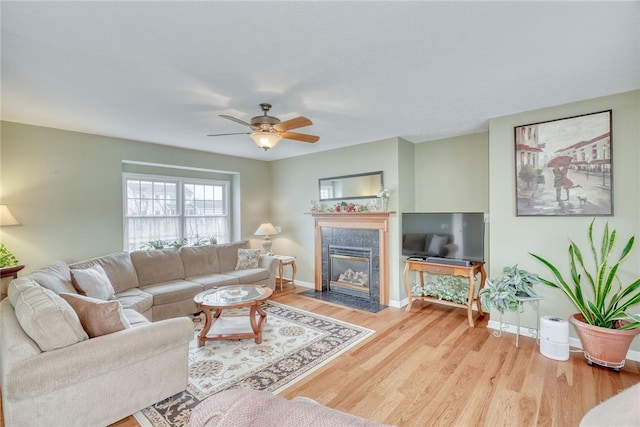 living room with a fireplace, a ceiling fan, baseboards, and wood finished floors