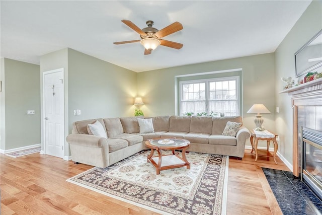 living area featuring a tiled fireplace, ceiling fan, light wood-type flooring, and baseboards