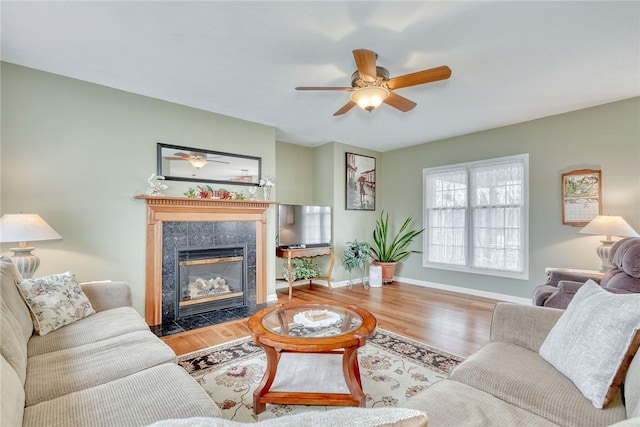 living room with ceiling fan, a fireplace, baseboards, and wood finished floors