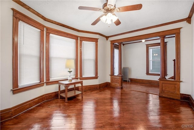 empty room featuring radiator heating unit, plenty of natural light, decorative columns, wood-type flooring, and crown molding