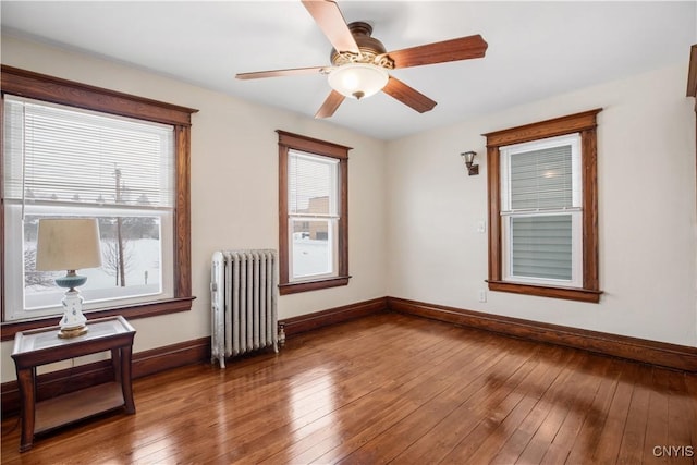 spare room featuring baseboards, wood-type flooring, ceiling fan, and radiator heating unit