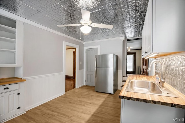 kitchen with an ornate ceiling, a sink, freestanding refrigerator, white cabinets, and wood counters