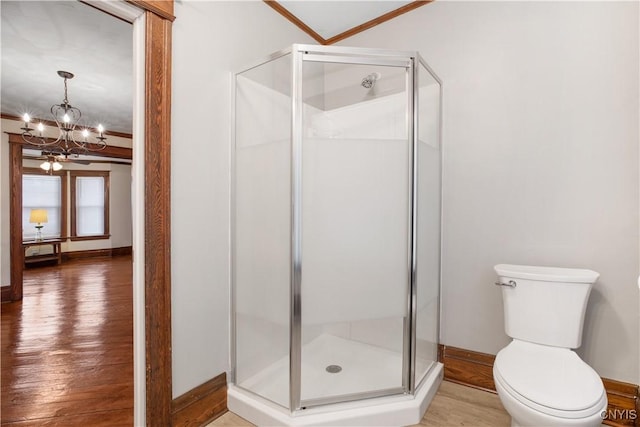 bathroom with a shower stall, a chandelier, toilet, ornamental molding, and wood finished floors