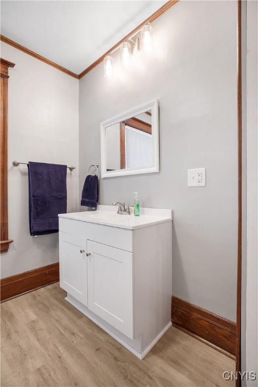 bathroom with vanity, crown molding, baseboards, and wood finished floors