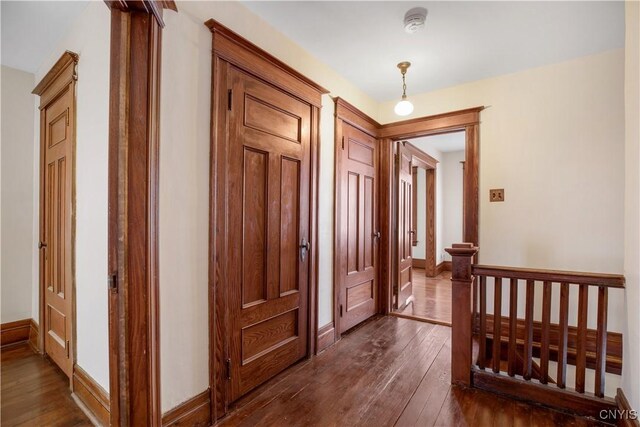 corridor with dark wood-type flooring, an upstairs landing, and baseboards