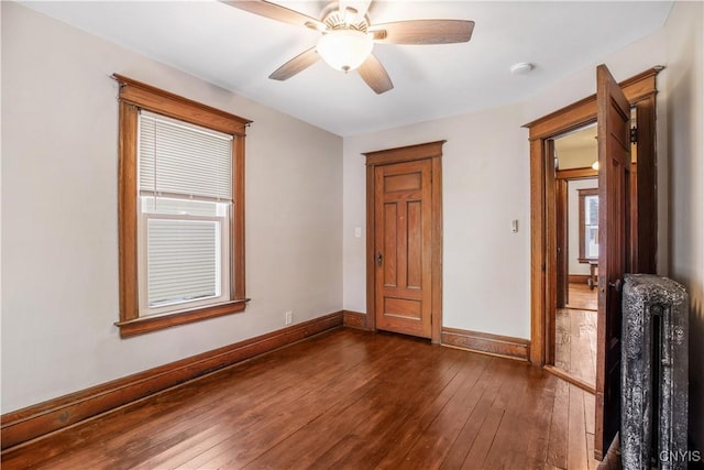 unfurnished bedroom featuring dark wood-type flooring, radiator heating unit, a ceiling fan, and baseboards