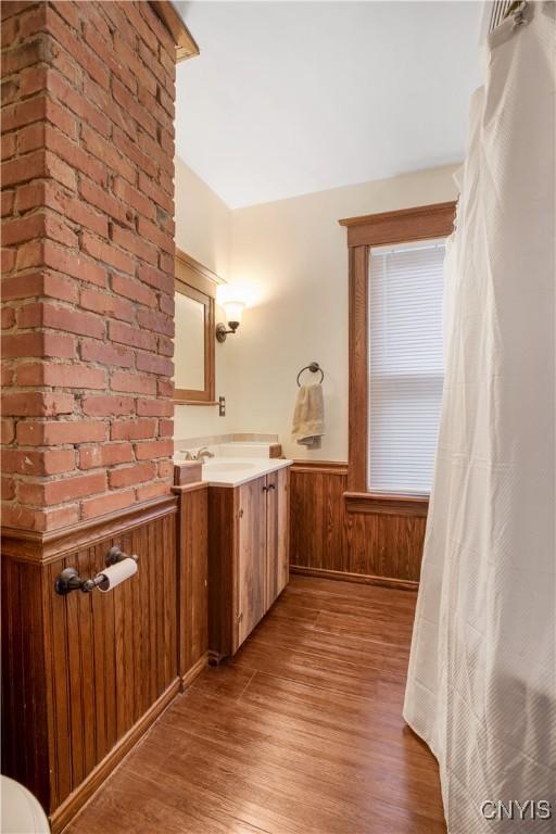 bathroom featuring vanity, wooden walls, wood finished floors, and wainscoting