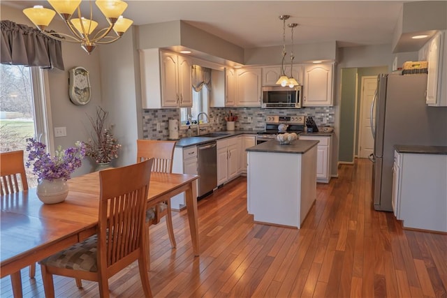 kitchen with wood finished floors, stainless steel appliances, dark countertops, backsplash, and a center island