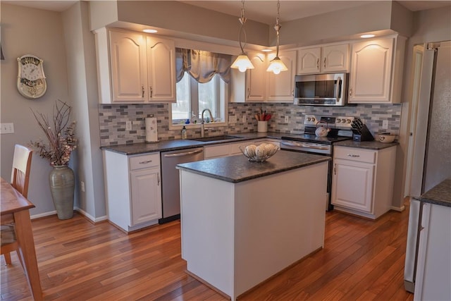 kitchen with hardwood / wood-style flooring, a sink, dark countertops, white cabinetry, and stainless steel appliances