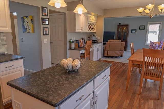 kitchen featuring tasteful backsplash, a center island, a chandelier, wood finished floors, and white cabinets