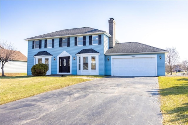 colonial home featuring driveway, an attached garage, a chimney, and a front lawn