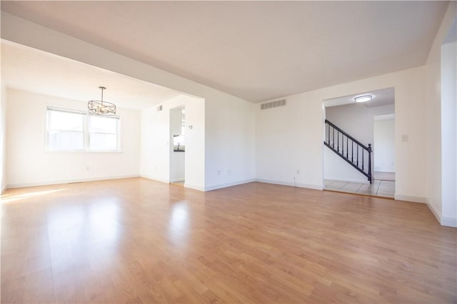 spare room featuring visible vents, a notable chandelier, light wood finished floors, baseboards, and stairs