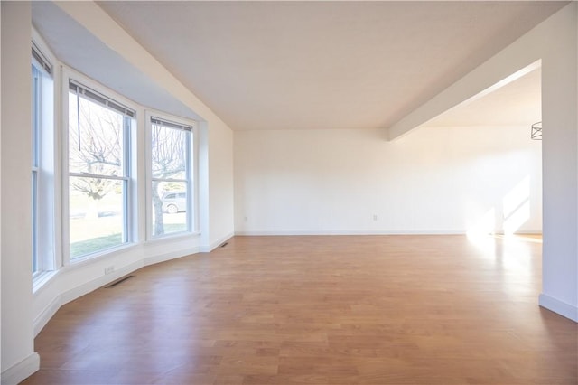 empty room with light wood-style floors, visible vents, and baseboards