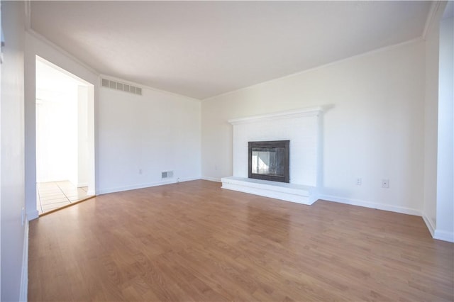 unfurnished living room with visible vents, wood finished floors, a fireplace, crown molding, and baseboards