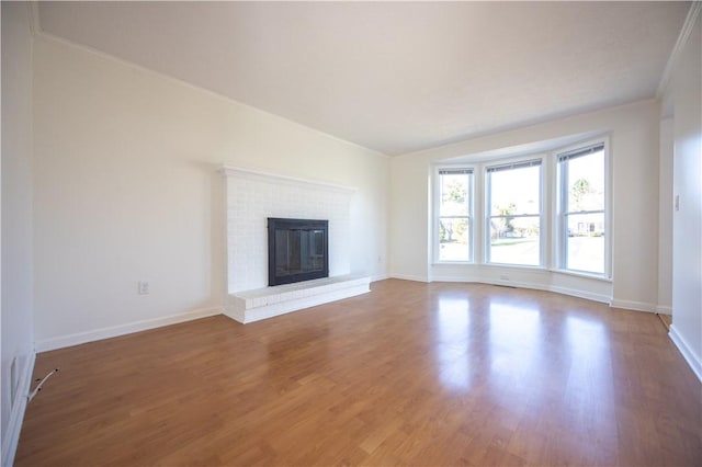 unfurnished living room with crown molding, a brick fireplace, wood finished floors, and baseboards