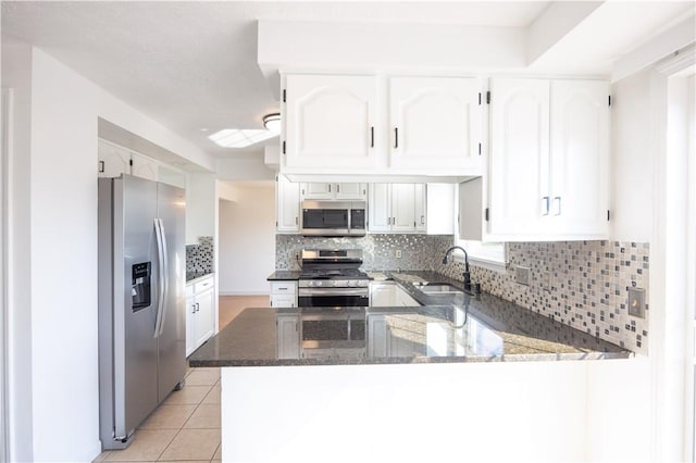 kitchen with light tile patterned floors, dark stone countertops, appliances with stainless steel finishes, a peninsula, and a sink