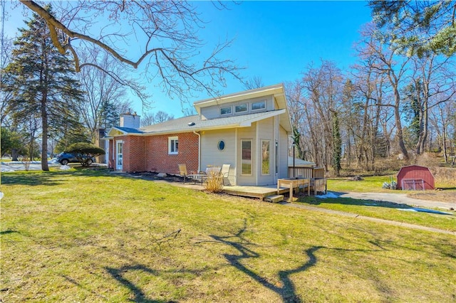 rear view of house featuring a yard, an outdoor structure, a wooden deck, brick siding, and a chimney