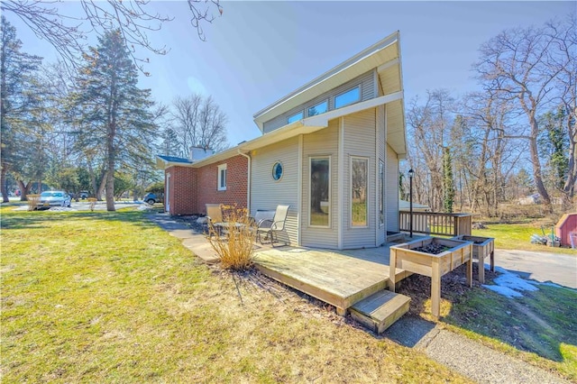 rear view of property featuring a deck, a lawn, and brick siding