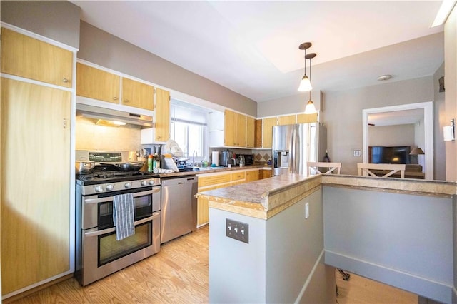 kitchen with under cabinet range hood, decorative light fixtures, light wood-type flooring, light countertops, and stainless steel appliances