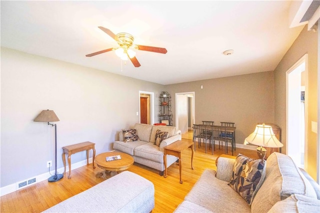 living room with visible vents, ceiling fan, baseboards, and light wood-style floors