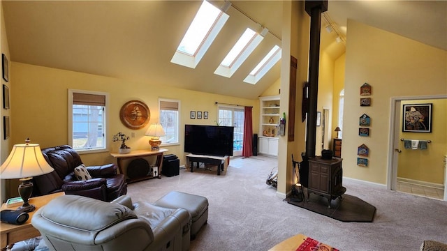 living room featuring carpet, baseboards, high vaulted ceiling, a wood stove, and a skylight