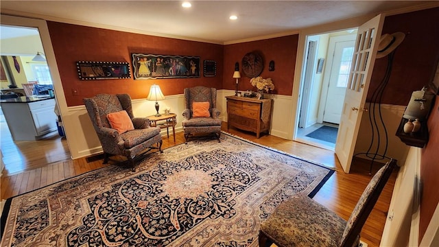 sitting room with ornamental molding, recessed lighting, wood-type flooring, and wainscoting